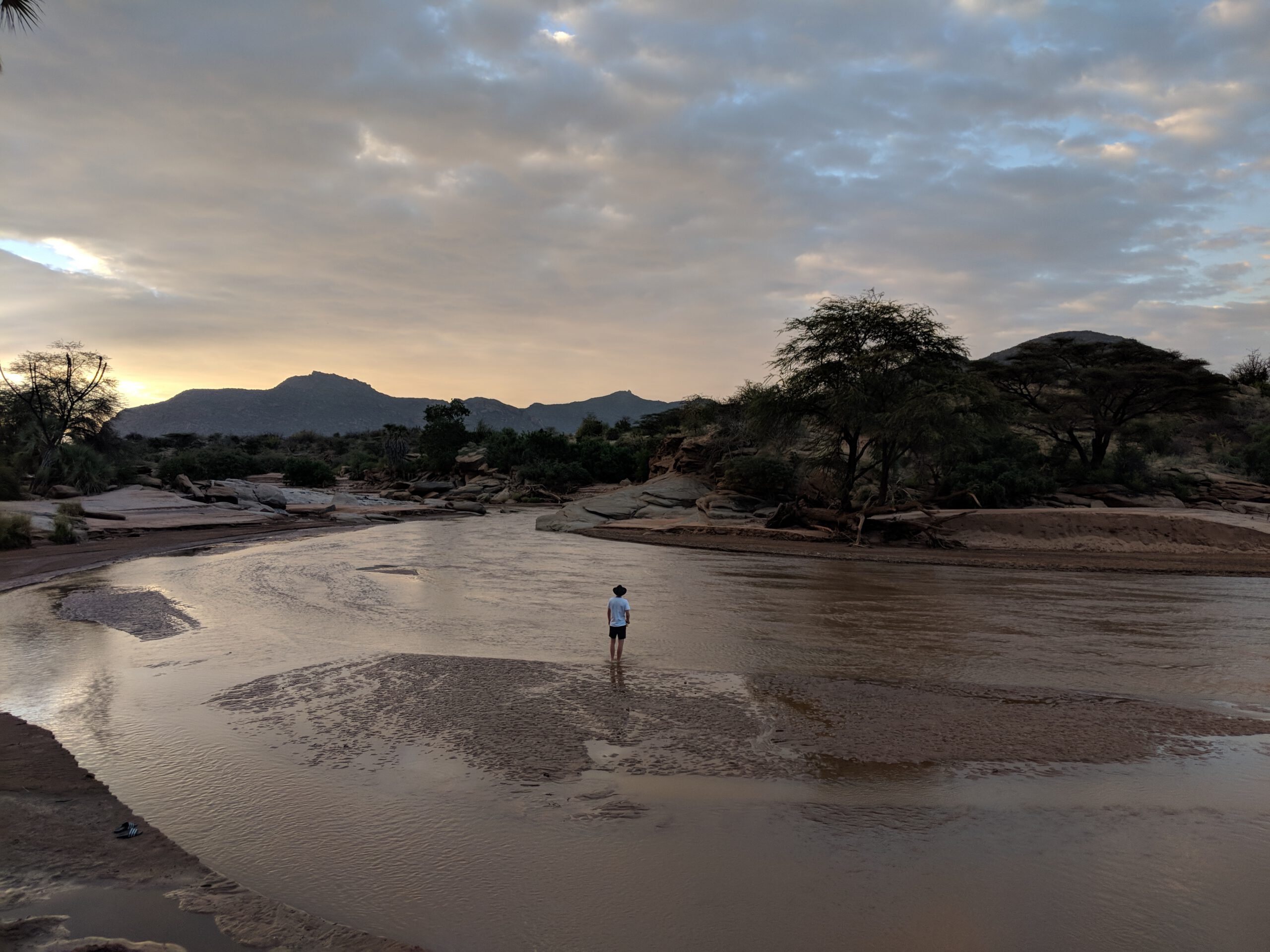 Motorbike rider standing by a river in northern Kenya at sunset