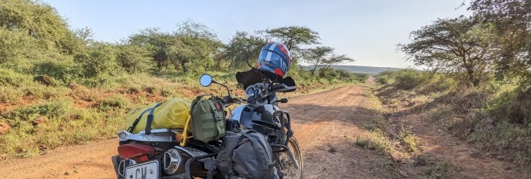 Adventure motorbike parked on a remote gravel road in Kenya surrounded by bushland and morning light