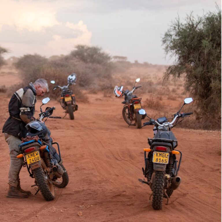 Riders with their motorbikes on a red dirt track in Kenya during a Safari MotoXpedition tour