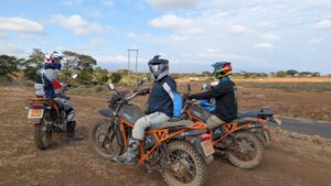 Riders on Kibo 250 motorbikes on a dirt road in southern Kenya with Mount Kilimanjaro behind