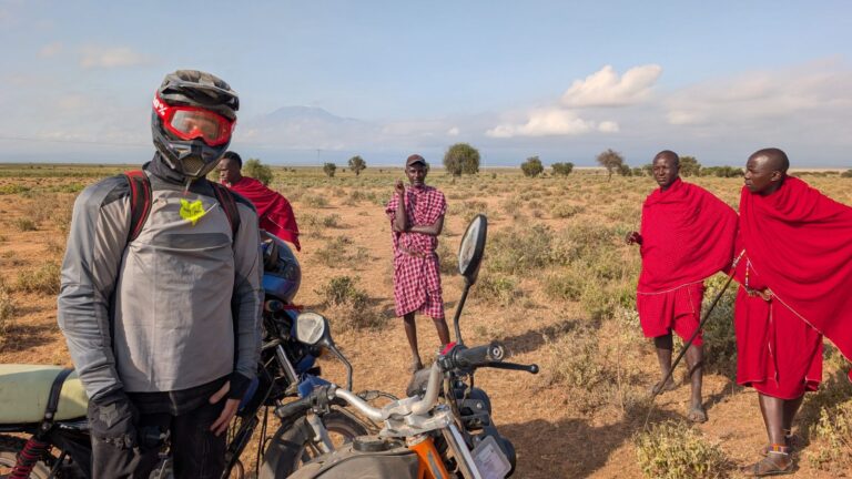 Motorbike rider meeting Maasai men on the plains of southern Kenya with Kilimanjaro in the background