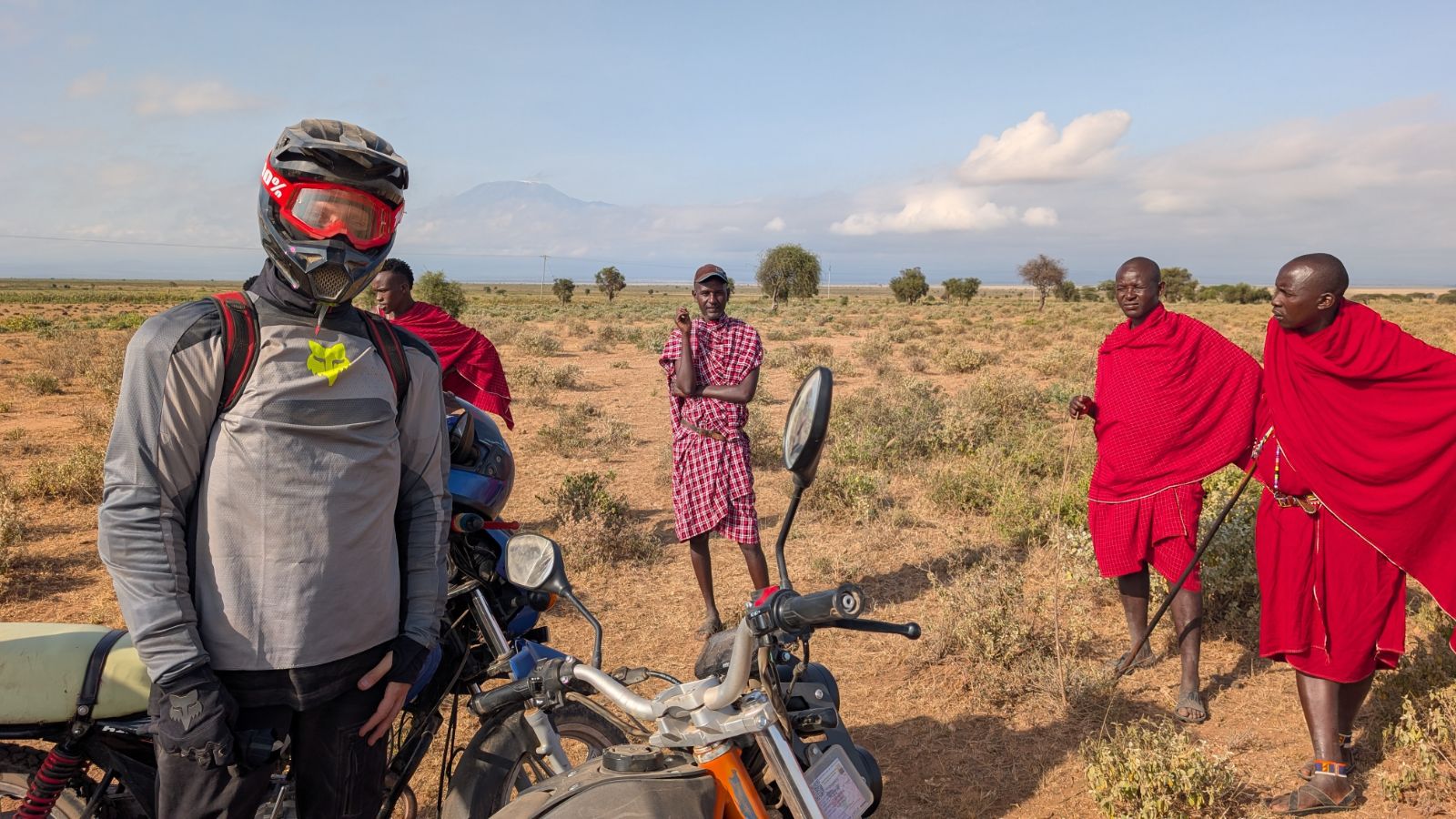 Motorbike rider meeting Maasai men on the plains of southern Kenya with Kilimanjaro in the background